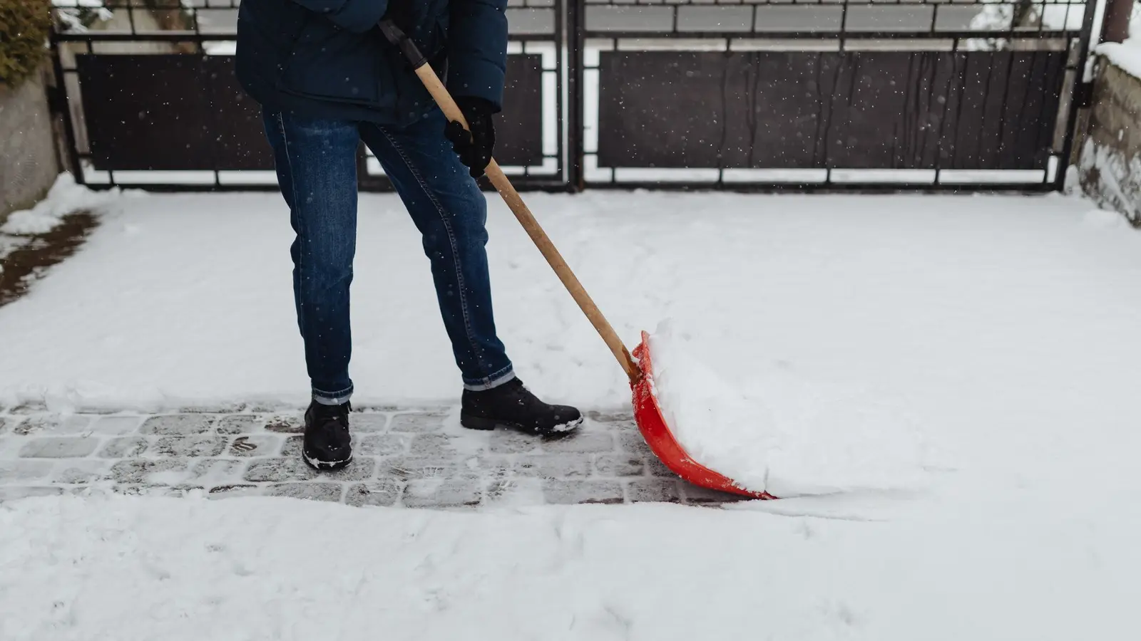 Person shoveling snow off a paved brick path