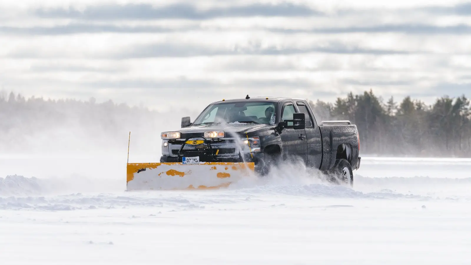 Pickup truck with a yellow plow blade pushing deep snow across an open lot