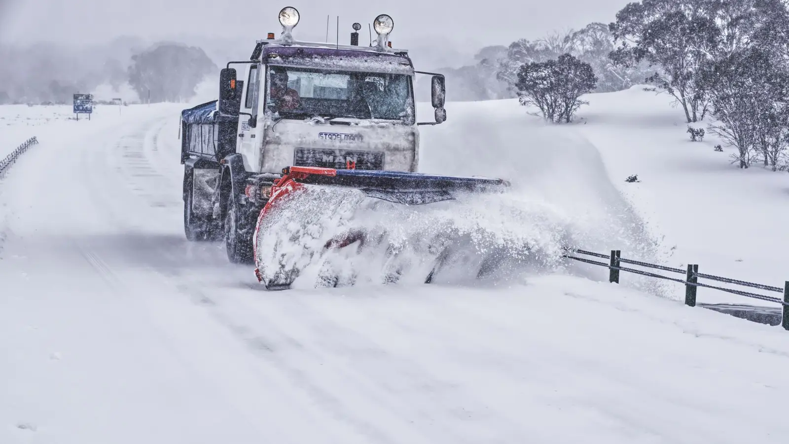 Large plow truck clearing a snow-covered road through open countryside