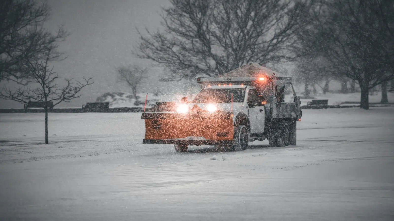 Plow truck with amber lights clearing a snow-covered lot at dusk