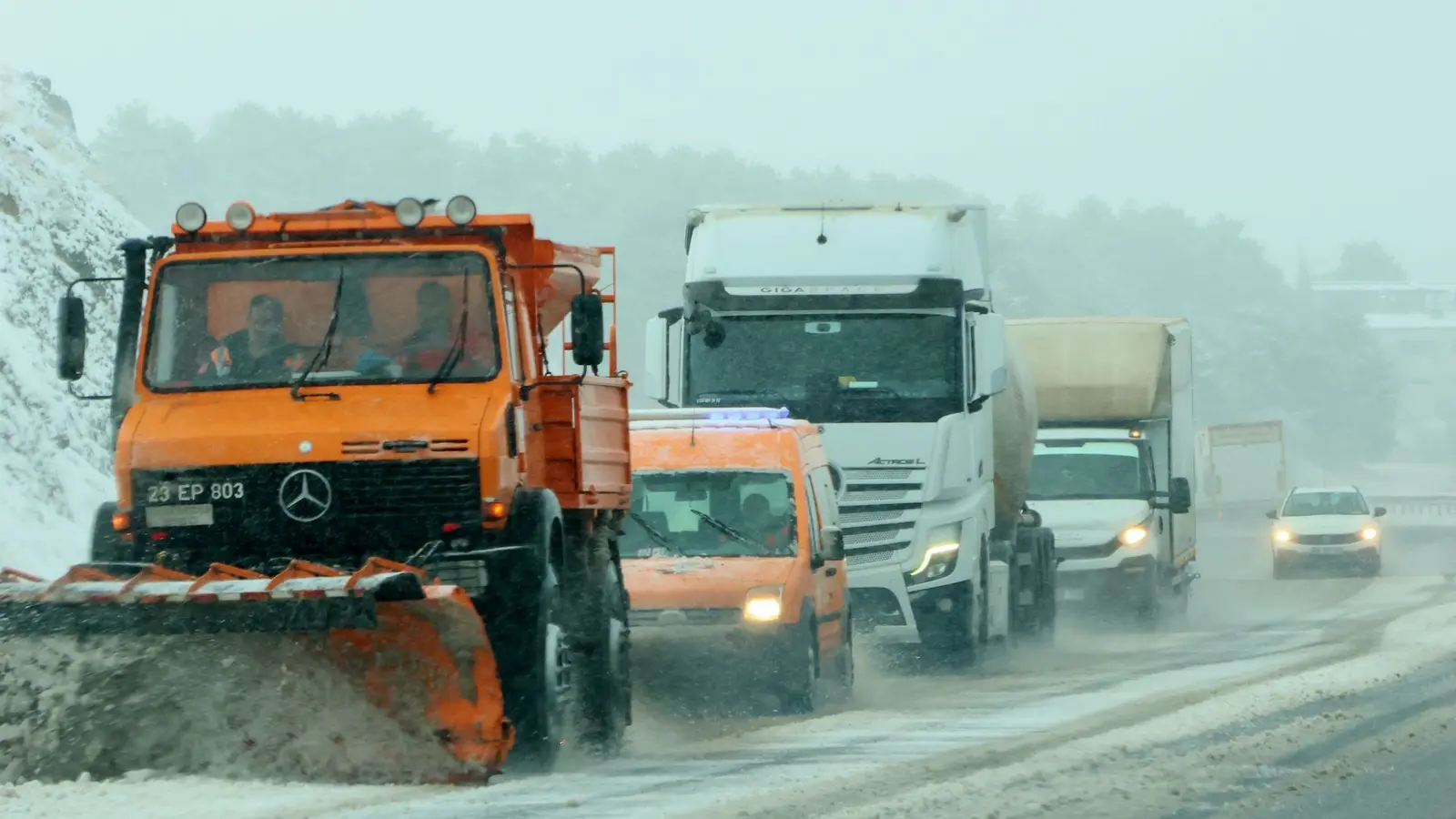 Line of plow trucks clearing a snowy highway