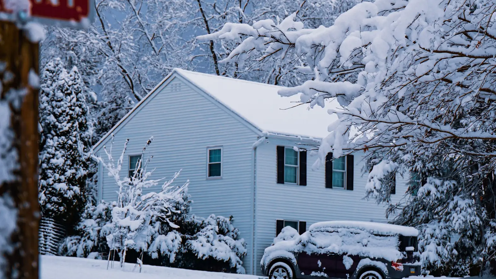 White house and SUV covered in fresh snow under heavy, snow-laden trees