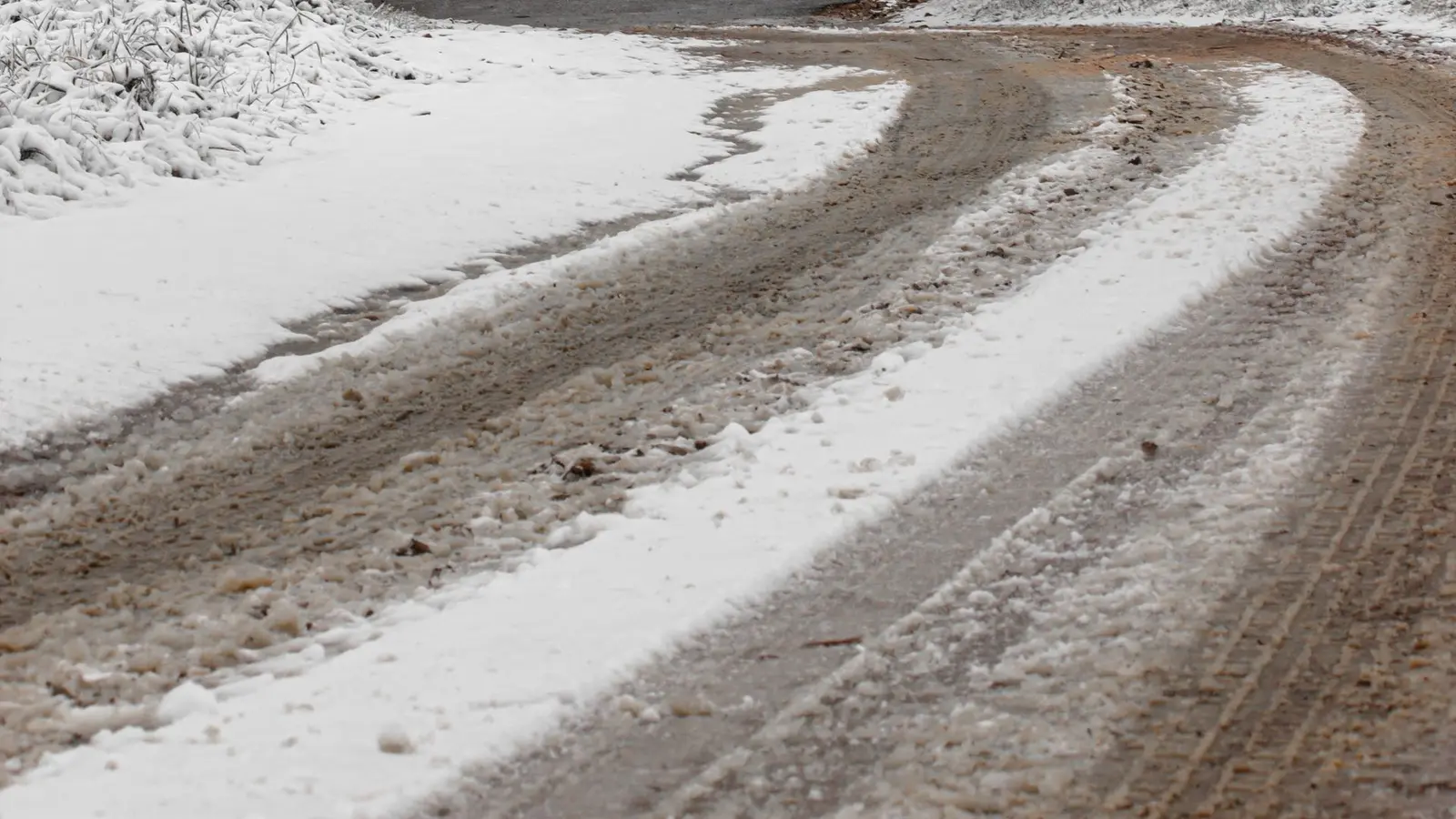 Snow-covered country road with a stop sign and bare trees