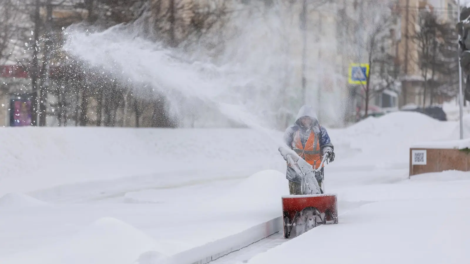 Worker in a high-visibility vest clearing a sidewalk with a snowblower